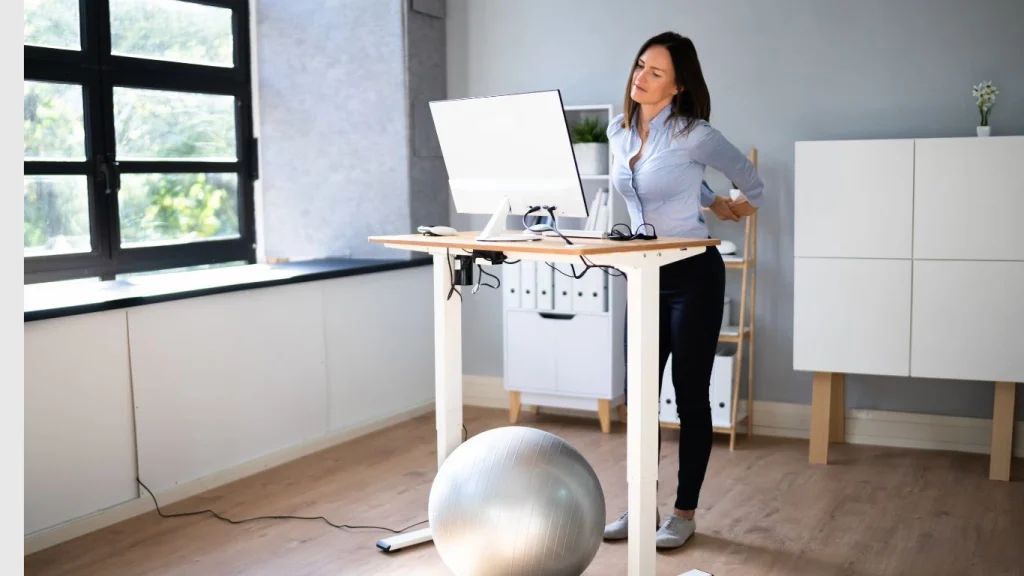 Woman experiencing back pain while working at a standing desk in a healthy home workspace setup