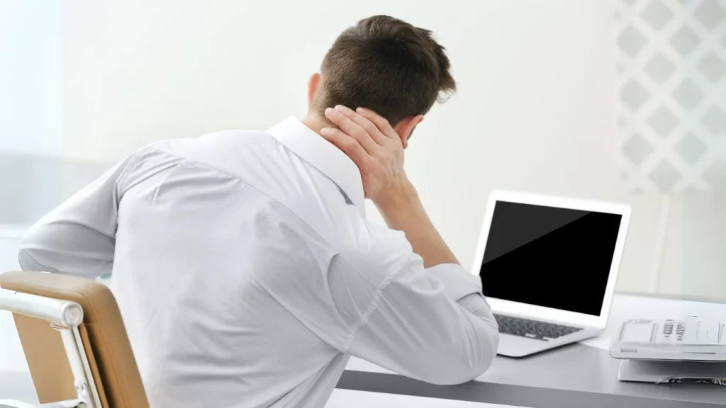 Office worker experiencing neck pain due to poor posture while working on laptop